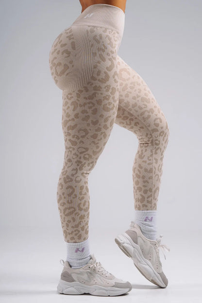 Person wearing beige leopard print leggings with white sneakers on a light gray background